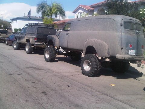 1986 Ford Bronco - A heavily modified panel van and a lifted SUV are parked on a street, both oversized tires and lifted suspensions.