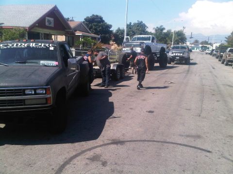 1986 Ford Bronco - Modified pickup trucks and trailers are parked on a street with people around them.