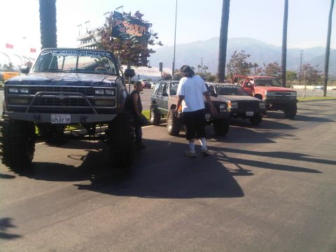 1986 Ford Bronco - Several modified trucks and SUVs are parked in a lot under palm trees.