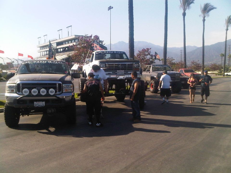 Several lifted trucks and SUVs parked in a lot with a grandstand in the background