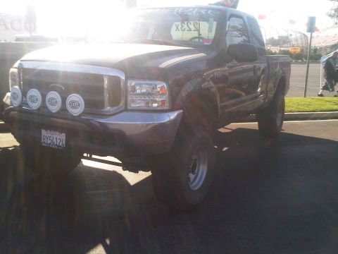 1986 Ford Bronco - A dark Ford F-250 Super Duty pickup truck is parked outdoors with a custom front bumper and auxiliary lights.