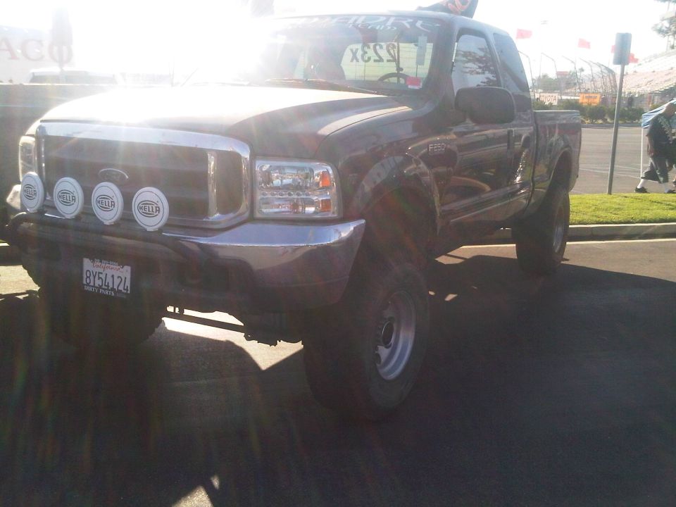 Dark pickup truck with chrome grille and four Hella lights, lifted suspension, and aftermarket wheels