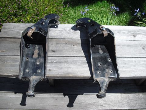 1986 Ford Bronco - Two black metal coil bucket mounts are shown resting on a wooden surface outdoors.