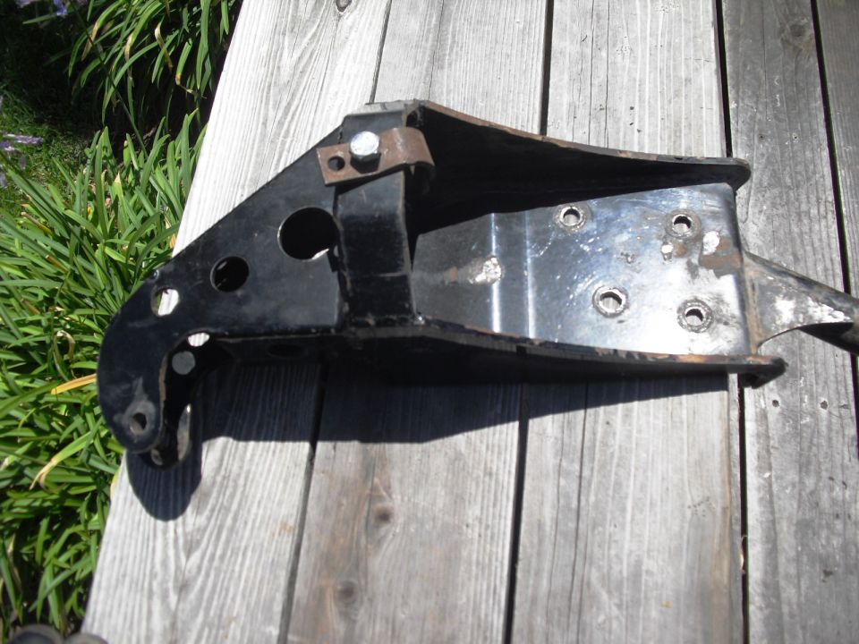 Black metal suspension part with holes and bolts, resting on wooden planks