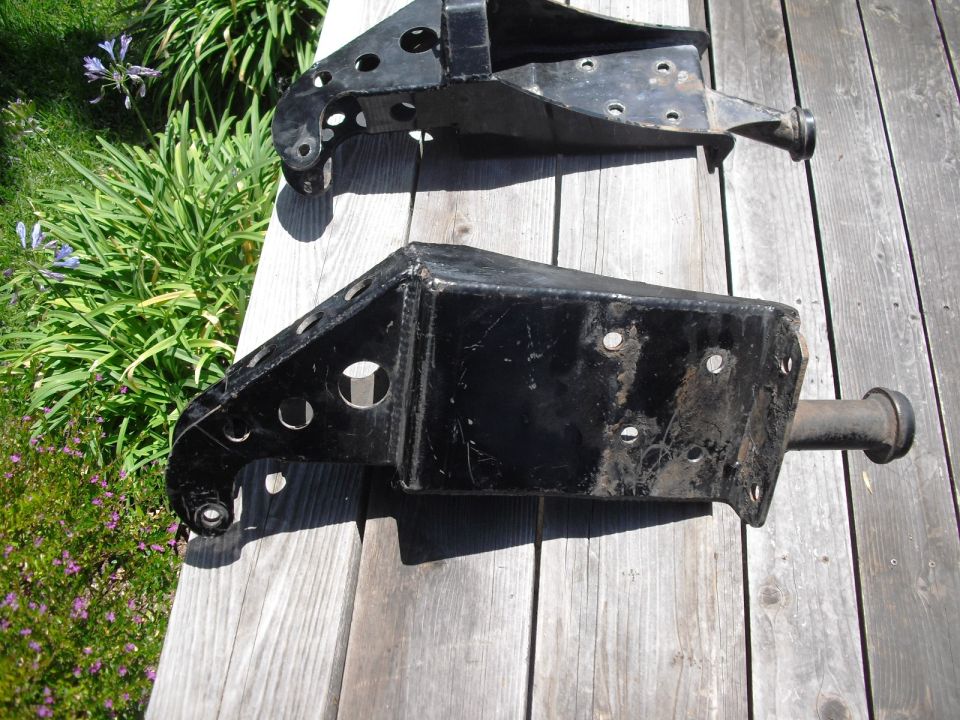 Two black metal automotive suspension components on a wooden surface