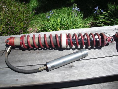 1986 Ford Bronco - Coilover shock absorber with remote reservoir shown on wooden planks outdoors.