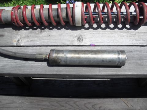 1986 Ford Bronco - A disassembled coilover shock absorber and its remote reservoir sit on wooden planks.
