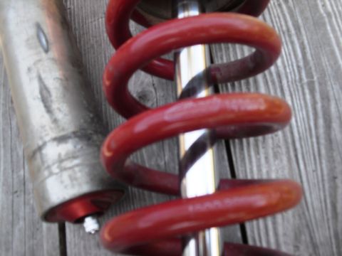 1986 Ford Bronco - Close-up of a red coilover shock absorber, a component for a vehicle's suspension system.