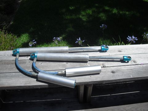 1986 Ford Bronco - Four shock absorbers are laid out on a wooden bench with grass and flowers in the background.