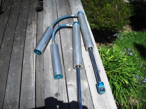 1986 Ford Bronco - Four aftermarket shock absorbers with blue accents and hoses are displayed on a weathered wooden deck.