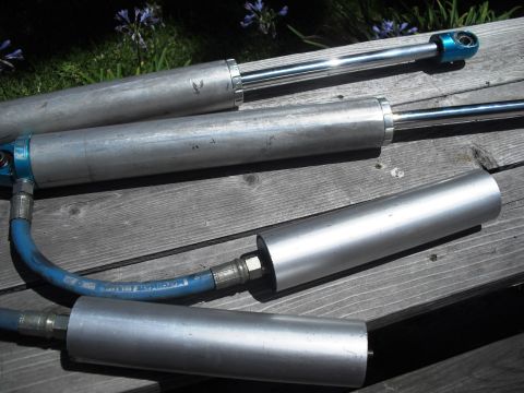 1986 Ford Bronco - Close-up of multiple shock absorbers, some with blue hoses, resting on a weathered wooden surface.