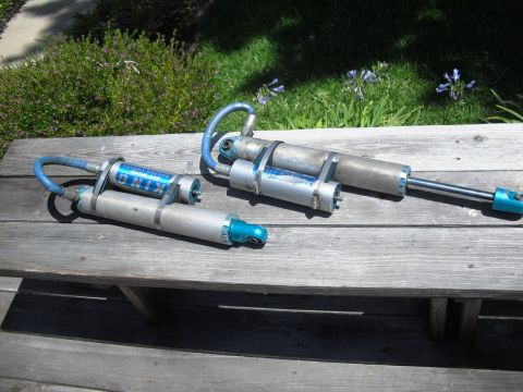 1986 Ford Bronco - Two King Off-Road Racing shocks are displayed on a weathered wooden table outdoors.