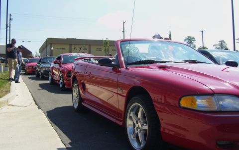 2007 Ford Mustang - A line of Mustangs are parked on a sunny day, with people standing on the sidewalk.
