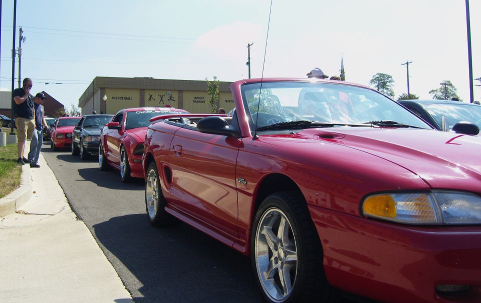Red convertible Mustang from the mid-1990s, parked in a line of cars. The car is clean and has aftermarket wheels
