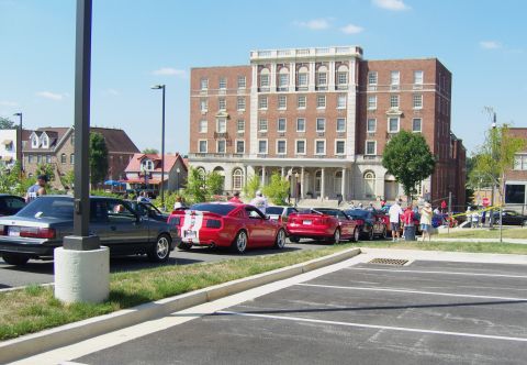 2007 Ford Mustang - Several Ford Mustangs are gathered in a parking lot outside a large brick building.