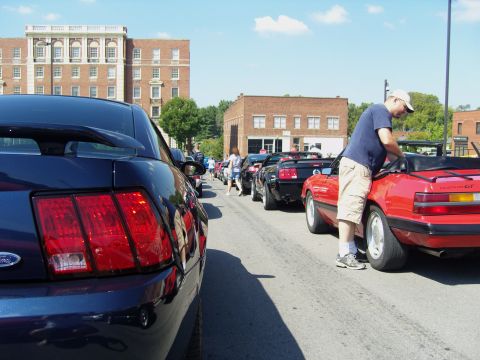 2007 Ford Mustang - A line of Ford Mustangs parked on a street, with a man attending to a red convertible.