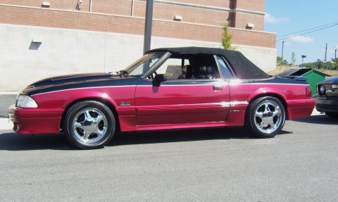2007 Ford Mustang - A two-tone red and black convertible Mustang is parked on the street, with another vehicle visible in the background.