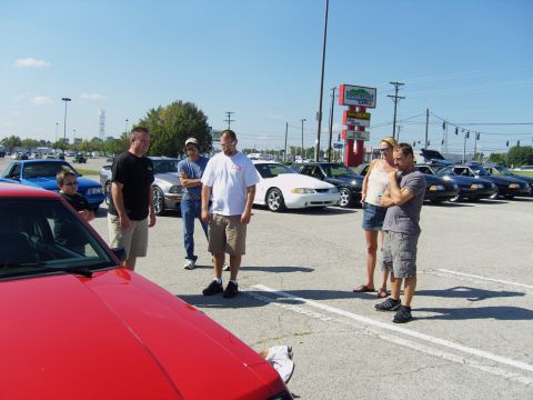2007 Ford Mustang - A group of people stand around multiple Ford Mustangs parked in a lot on a sunny day.