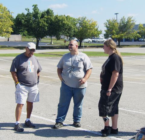 2007 Ford Mustang - Three men stand in a parking lot, conversing under a clear sky with trees and buildings in the background.