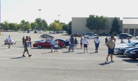 2007 Ford Mustang - A gathering of people and vehicles in a large outdoor parking area on a sunny day.