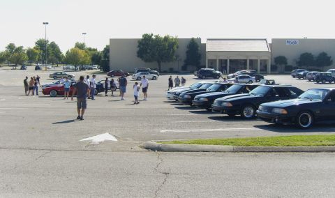2007 Ford Mustang - Several Ford Mustangs are gathered in a parking lot outside a shopping center.