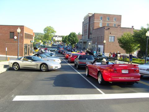 2007 Ford Mustang - A street lined with various cars, including a red convertible Mustang GT, during a car show event.