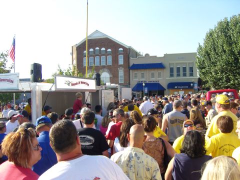 2007 Ford Mustang - A large crowd of people are gathered on a street, with buildings and an American flag visible in the background.