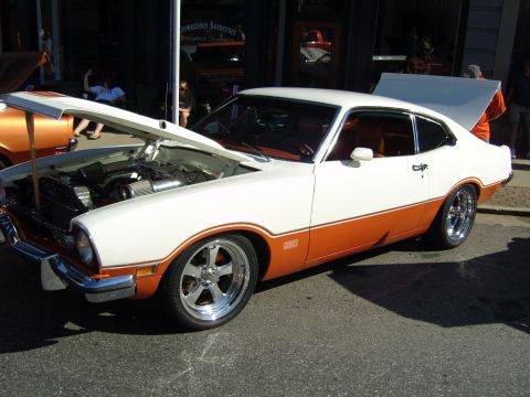 2007 Ford Mustang - A two-tone white and orange 1970 Ford Maverick is displayed with its hood and trunk open at an outdoor event.