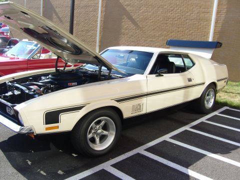 2007 Ford Mustang - A cream 1971 Ford Mustang Mach 1 is parked with its hood open, revealing the engine. Another red car is visible in the background.
