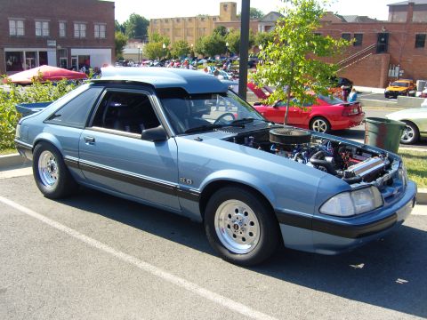 2007 Ford Mustang - A blue Ford Mustang is parked with its hood up, revealing the engine, at an outdoor car show.