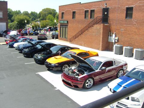 2007 Ford Mustang - A collection of Ford Mustangs are displayed with their hoods open at an outdoor car show.