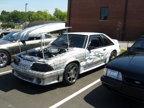 2007 Ford Mustang - A customized Ford Mustang with unique paintwork is displayed with its hood open, alongside other vehicles.