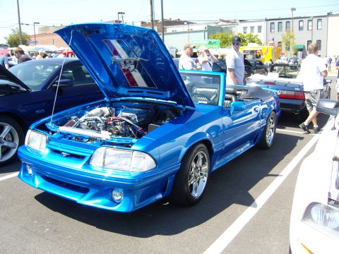 2007 Ford Mustang - A bright blue convertible is displayed with its hood open at an outdoor car show, revealing the engine.