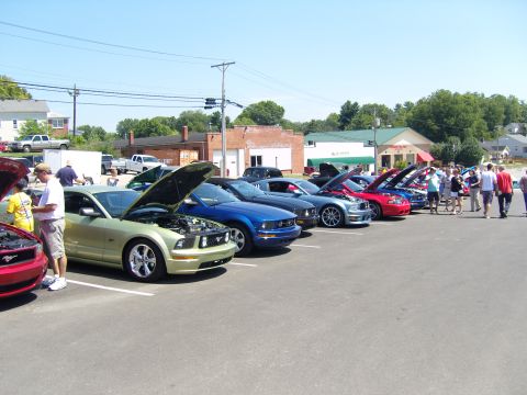 2007 Ford Mustang - A line of Ford Mustangs, mostly with hoods open, are parked in a lot on a sunny day.