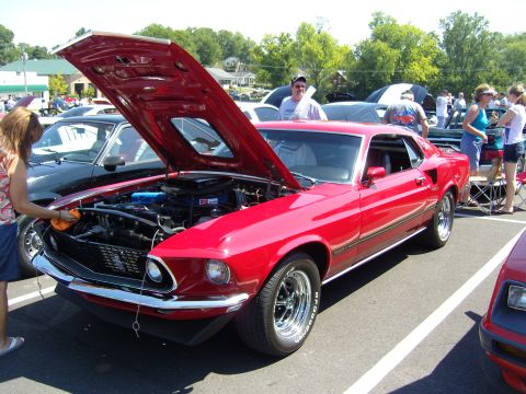 2007 Ford Mustang - A red 1969 Ford Mustang Mach 1 is displayed with its hood open, revealing the engine, while a person polishes the front.