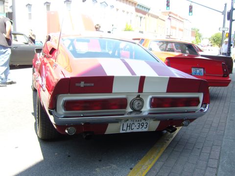 2007 Ford Mustang - The rear of a classic red and white striped Shelby GT500 is shown, parked on a street with other vehicles.
