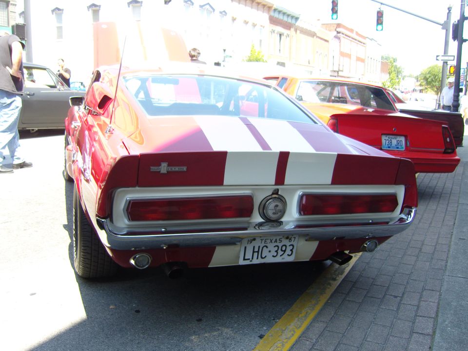 Red and white striped 1967 Shelby GT500 parked on street, another red car behind it