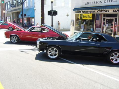 2007 Ford Mustang - Two classic American muscle cars, a black Camaro and a red Chevelle, displayed on a street with their hoods open.