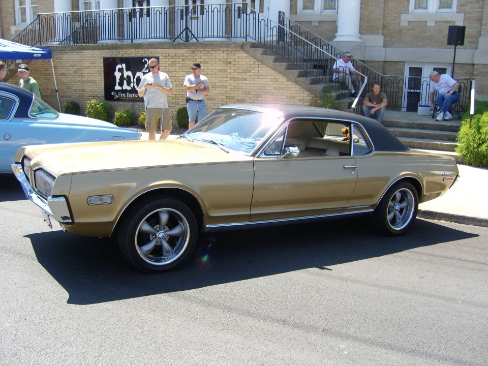 Gold Mercury Cougar with a black vinyl top parked on the street next to a blue car