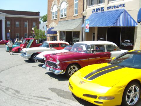 2007 Ford Mustang - A line of vintage cars and a modern yellow sports car are parked on a street in front of a business.