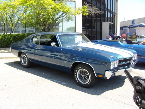 2007 Ford Mustang - A blue 1970 Chevrolet Chevelle SS muscle car with white racing stripes is parked in front of a modern building.