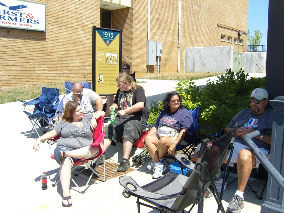People sit in lawn chairs outside a brick building with a sign that reads "First & Farmers National Bank"