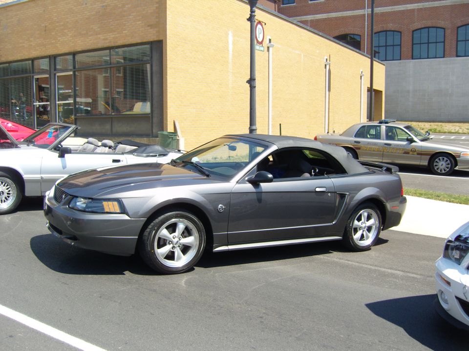 Dark gray convertible with a black top, viewed from the side. The car has a silver trim line along the bottom and five-spoke wheels