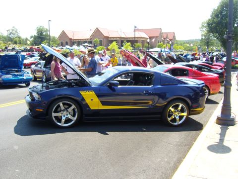 2007 Ford Mustang - A blue 2007 Ford Mustang with a yellow stripe is displayed with its hood open at a car show.