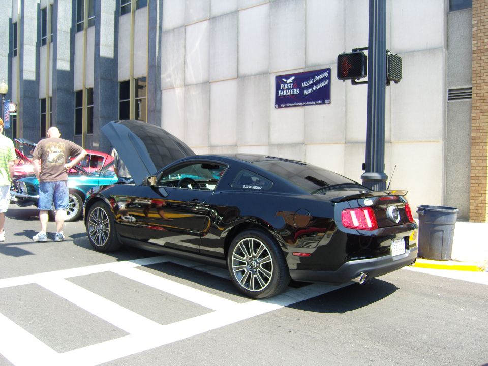 Black Ford Mustang with hood open, viewed from the rear quarter, parked on a street with crosswalk