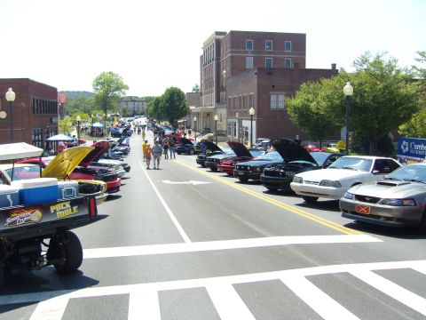 2007 Ford Mustang - A street car show features numerous Ford Mustangs lined up, with several hoods open.