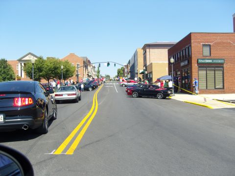 2007 Ford Mustang - A street lined with Ford Mustangs and onlookers under a clear blue sky.
