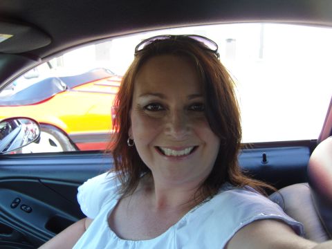2007 Ford Mustang - A woman smiles from the driver's seat of a 2007 Ford Mustang, with another orange Mustang convertible visible through the window.