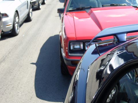 2007 Ford Mustang - A line of cars, including a red Fox Body Mustang, are parked on a street.