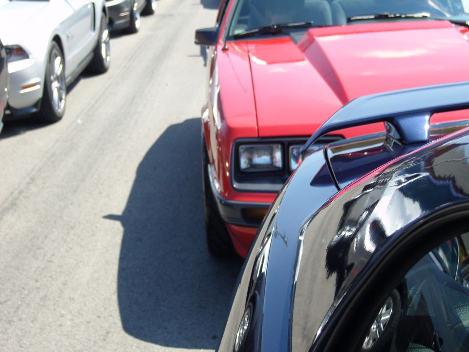 Red fox body Mustang in line with other cars. Blue spoiler on car in foreground
